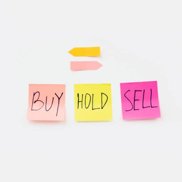 Three sticky notes with "BUY" (orange), "HOLD" (yellow), and "SELL" (pink)—common financial services terms—arranged in a row. Two arrow-shaped sticky notes, one orange and one yellow, sit above them on a white background.