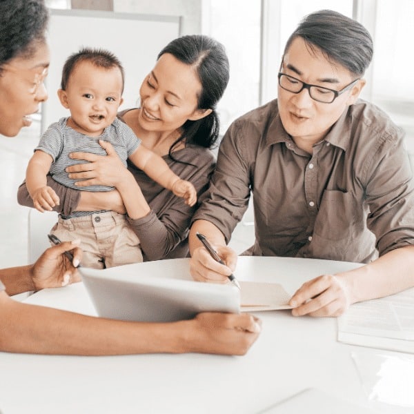 A smiling couple with a baby sit across from a professional woman at a desk, discussing insurance services from Spectre Financial. The woman holds a tablet, while the man holds a pen and paper, suggesting a friendly consultation or meeting.