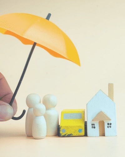 A hand holds a yellow umbrella over wooden figures representing a family, a car, and a house, symbolizing the protection offered by financial services Windsor for your home, vehicle, and loved ones.